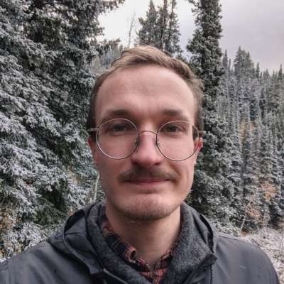 Jem with round-wire rimmed glasses and a mustache in snowy forest