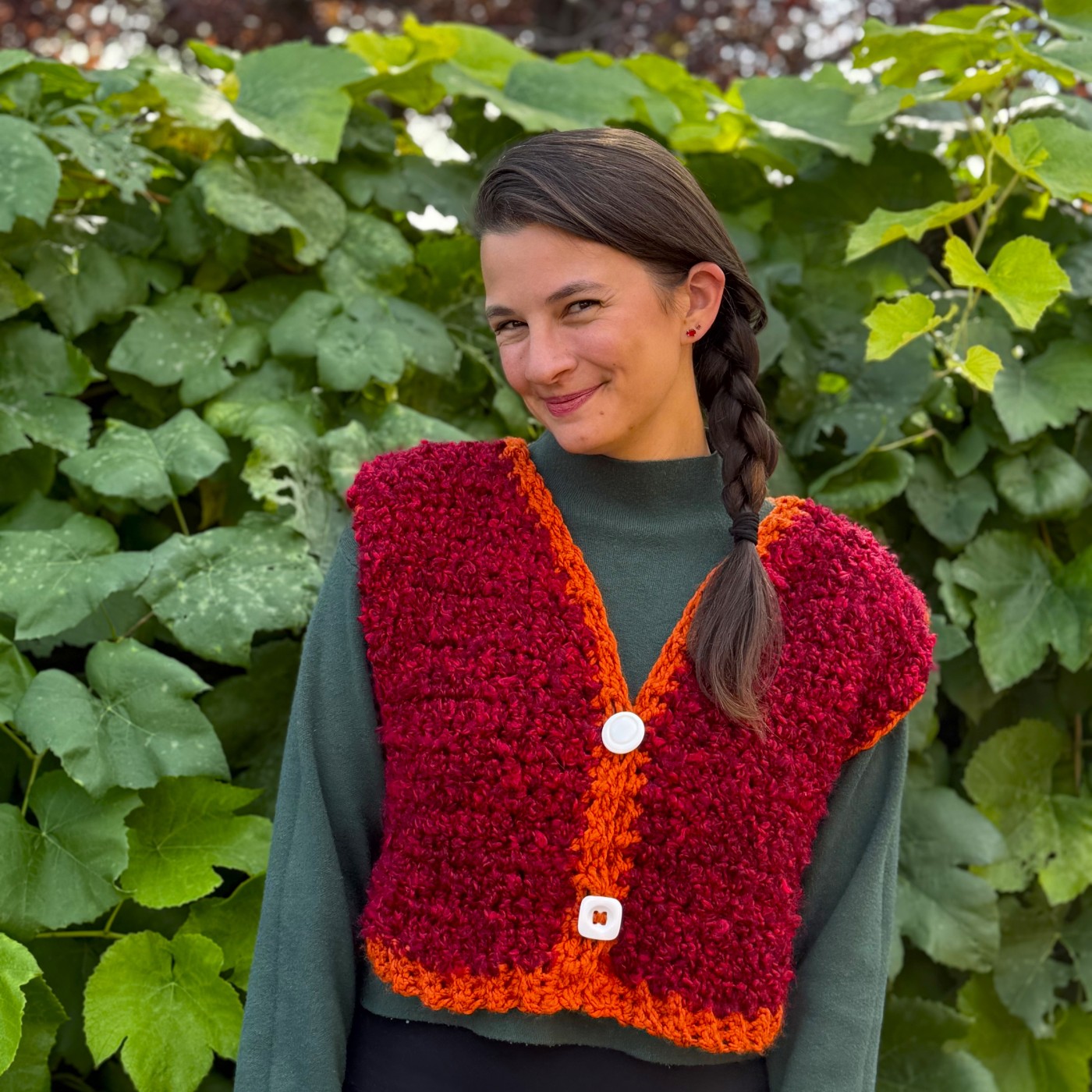 Kat wearing a red knit vest with nature in the background.