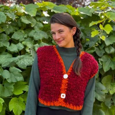 Kat wearing a red knit vest with nature in the background.