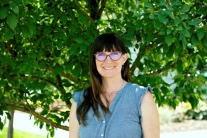 Photo of Amy May in blue shirt and red glasses