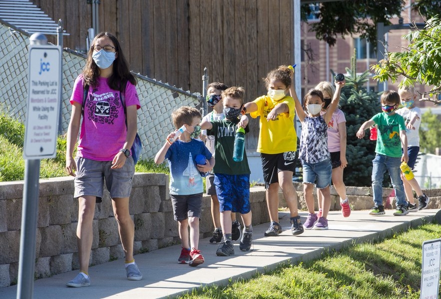 Kids in colorful shirts and masks walking single file