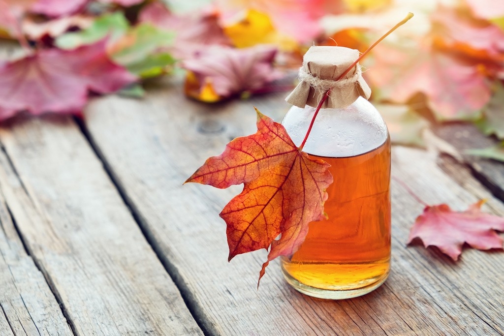 Maple syrup in jar on table with colorful maple leaves