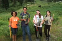 Four volunteers stand with small potted trees